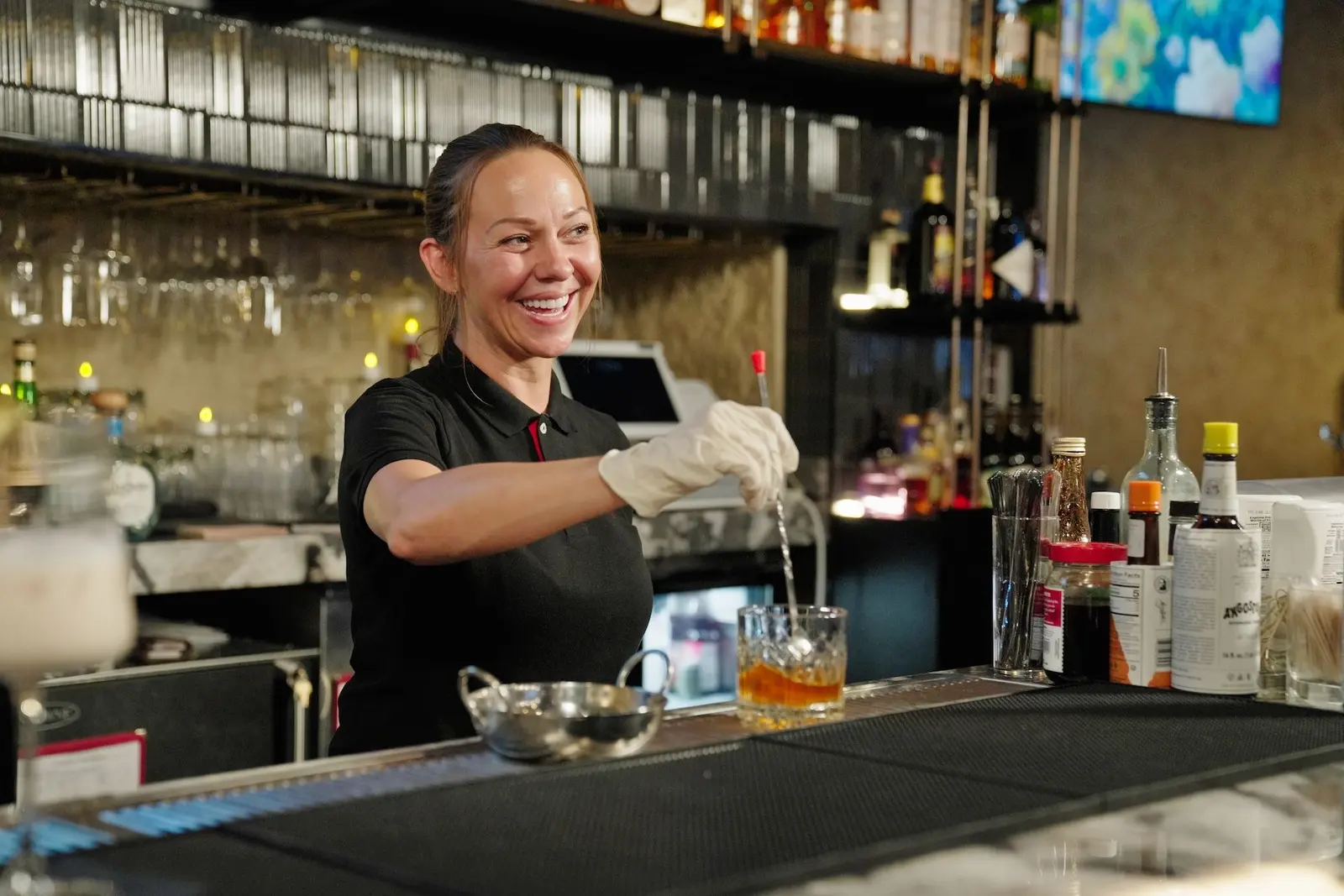 The bartender laughing as she builds a drink