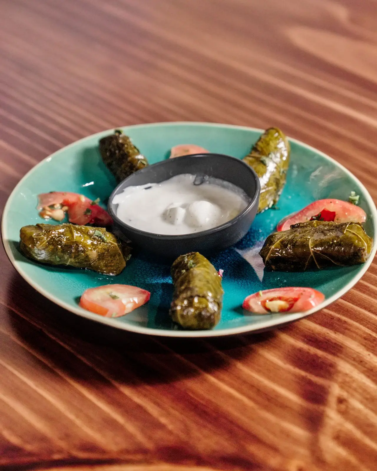Dolmeh around a yogurt dip on a teal plate