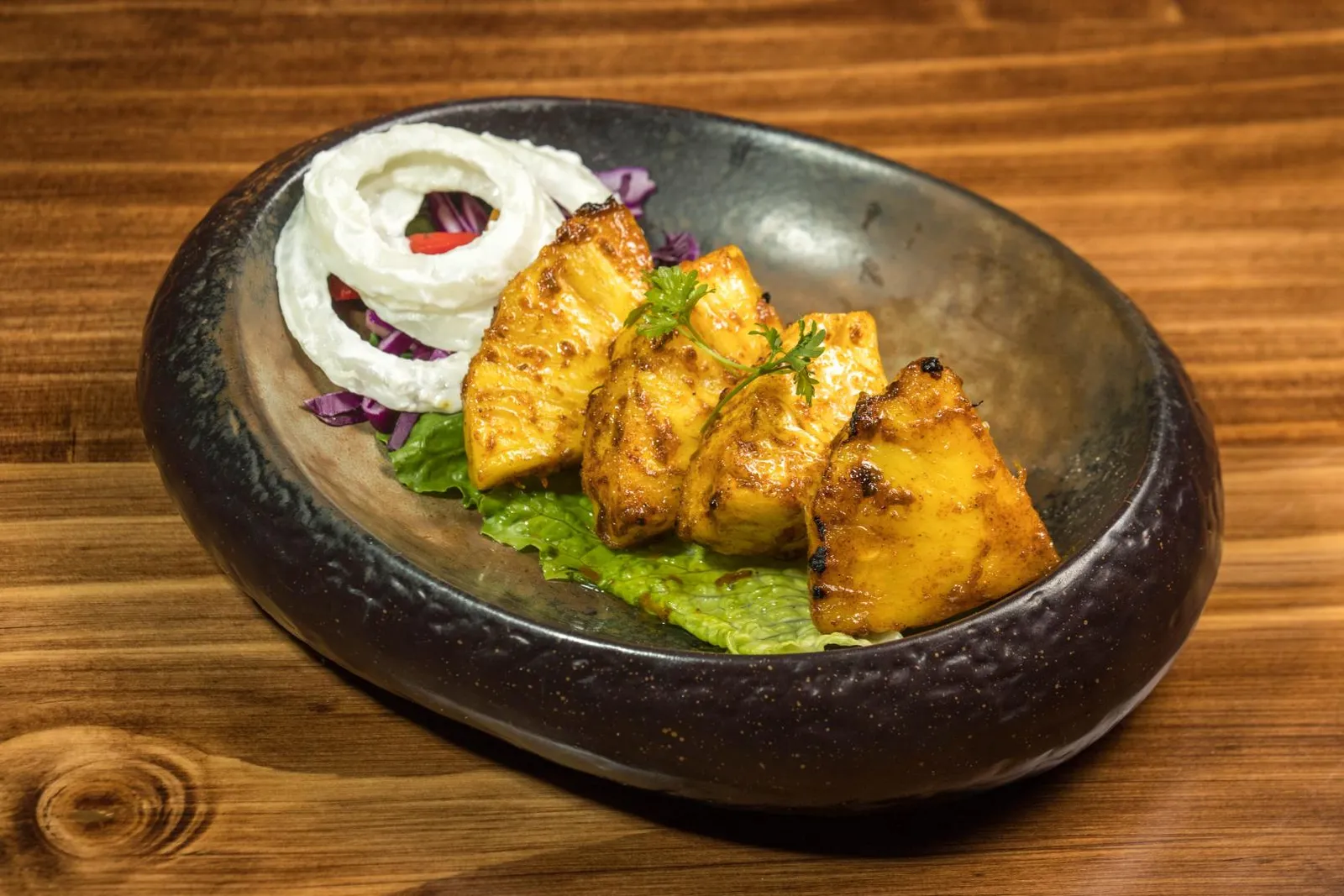 Pineapple tandoori in a dark stone bowl with onion rings and lettuce