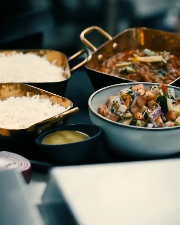 White rice, a curry and a chopped salad in brass and stoneware serving dishes